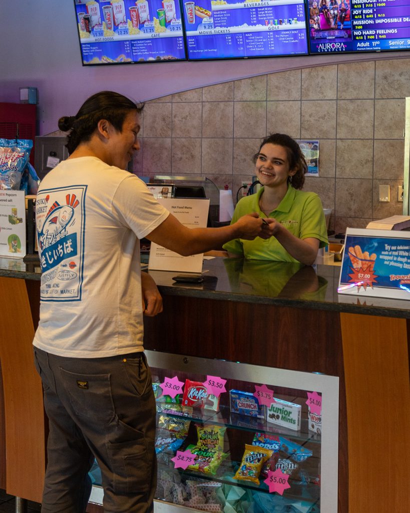 young woman smiling behind counter handing ticket to male customer