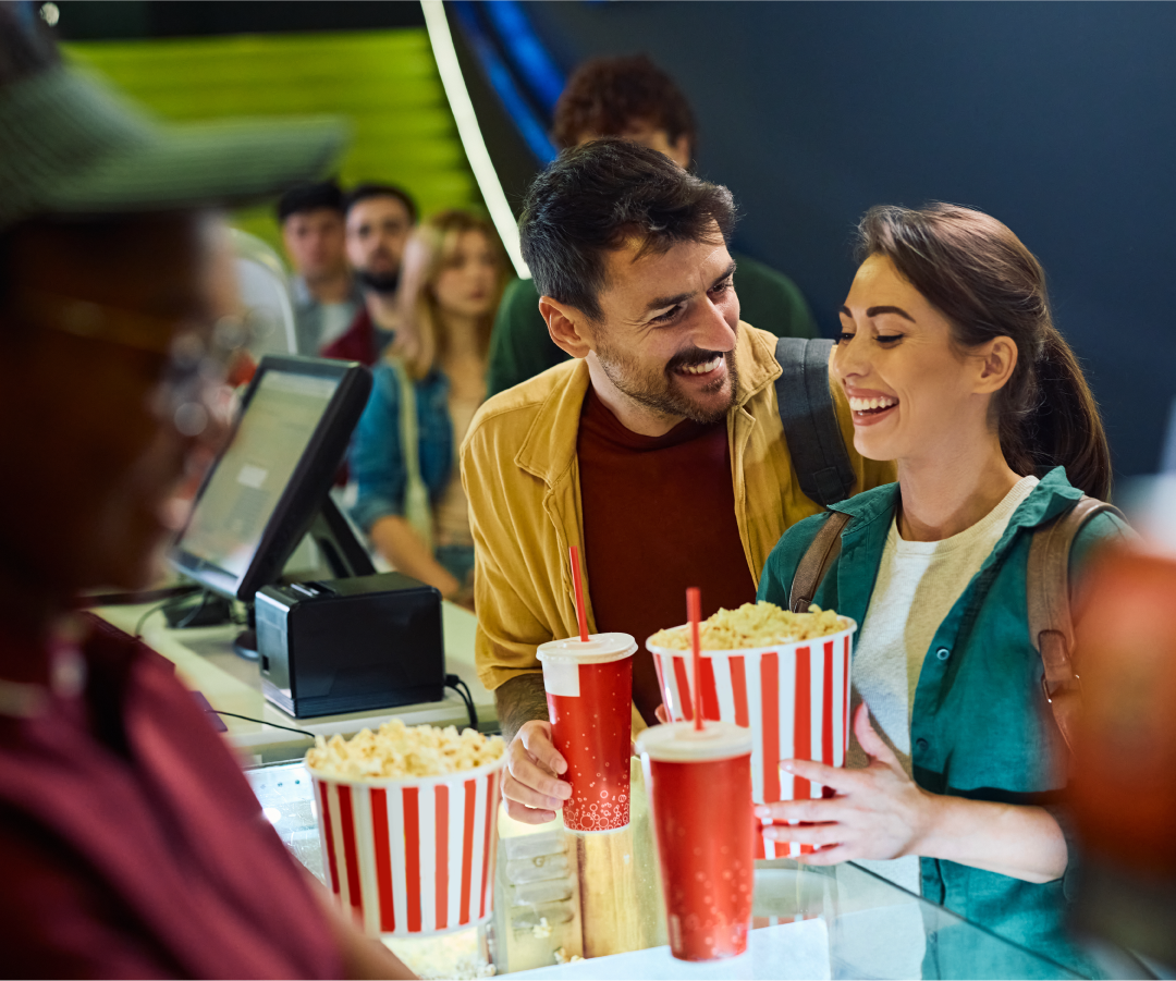 smiling man and woman holding popcorn and sodas at a concessions counter